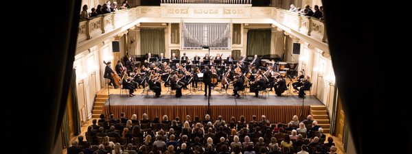 The Orchestra play in a concert hall as an audience watch one.