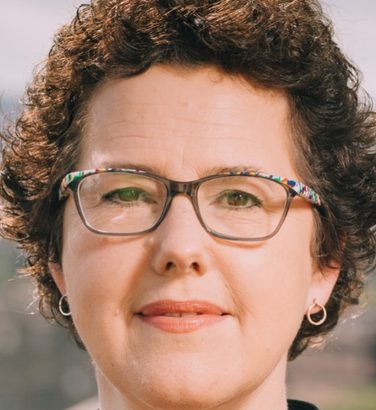 Close-up of Joanna Baker. She looks directly at the camera, smiling, wearing glasses.