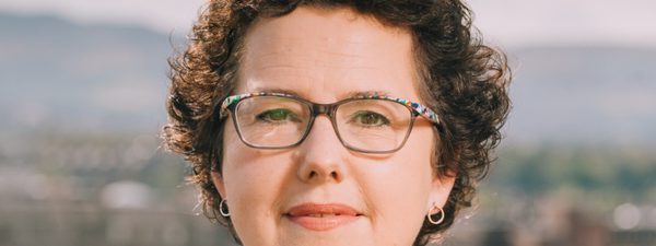 Close-up of Joanna Baker. She looks directly at the camera, smiling, wearing glasses.