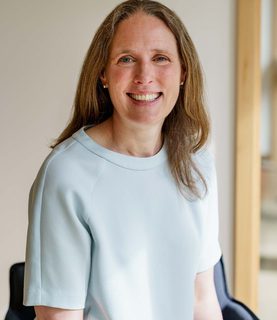 Sarah Davidson, wearing a light blue blouse, sits smiling at the camera.