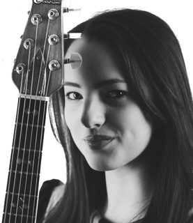 A black and white close up of Devin. She holds her guitar upright and you can see the top of it. She has straight dark hair.