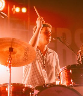 Phil plays the drums, he wears striped tshirt.