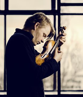 Violinist Pekka Kuusisto, eyes closed, holds his violin close to his face, plucking the strings with his fingers, as he looks down.