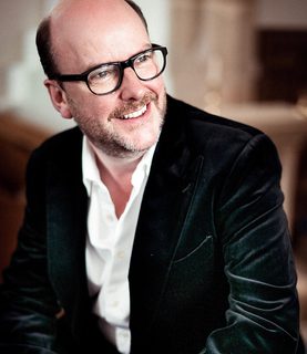 Bass-baritone Neal Davies, wearing glasses, laughs while looking towards the right of the image.