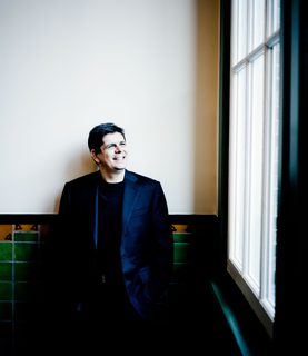 Javier stands and smiles by a large window.