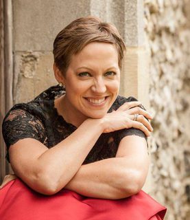 Soprano Julia Doyle sits, smiling with crossed arms, her right hand touching her left shoulder, chin resting on her hand.