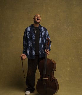 Sheku Kanneh-Mason stands with his cello, tilting his head back in laughter.