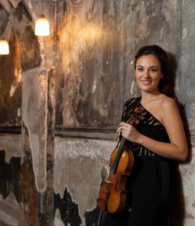 Violinist Nicola Benedetti leans against a wall, holding her violin.