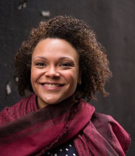 Rachel Redmond smiles to the camera. She wears a ed tunic like dress.