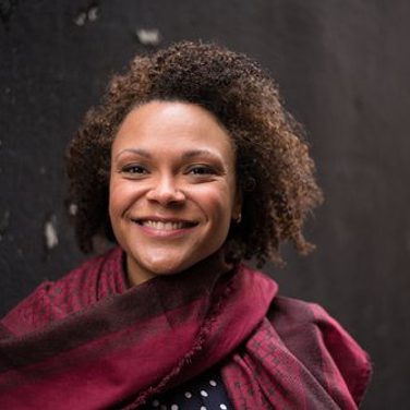 Rachel Redmond smiles to the camera. She wears a ed tunic like dress.