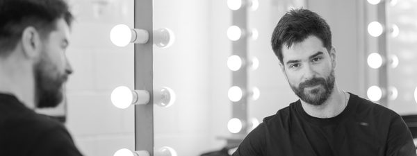 Bogdan looks into the dressing room mirror. He wears a black top and has his violin on the table top.
