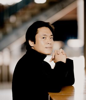 Sunwook Kim rests his arms on a piano, looking at the camera.