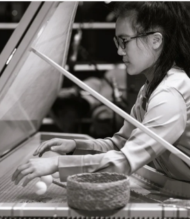 Tiffany plays the harpsichord. She wears black glasses. The photo is in greyscale.