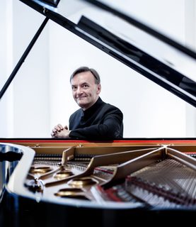 Sir Stephen Hough smiles directly at the camera, through the open piano lid.