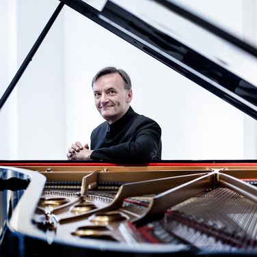 Sir Stephen Hough smiles directly at the camera, through the open piano lid.