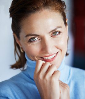 A headshot. Sylvia wears a light blue shirt and smiles. She had shoulder length brown hair.
