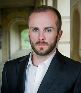 Tenor Thomas Walker stands in the hallway of an old building, leaning against a wall, looking directly into the camera.