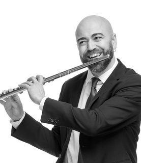Andre smils as he holds his flute up to play. He wears a dark suit.