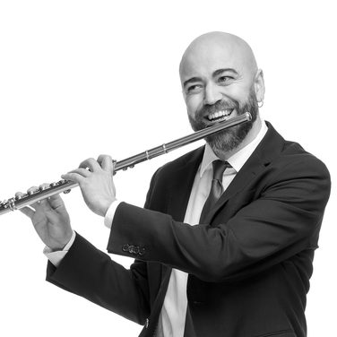Andre smils as he holds his flute up to play. He wears a dark suit.