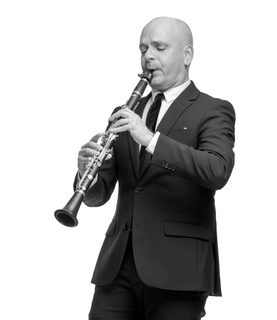 Maxi plays the clarinet. He wears a black suit and black tie.