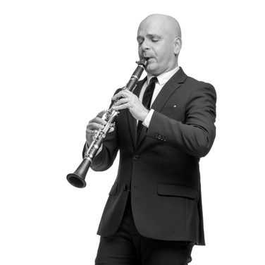 Maxi plays the clarinet. He wears a black suit and black tie.