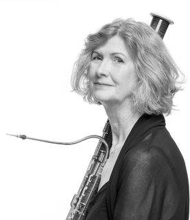 A head shot Alison with her bassoon resiting upright on her shoulder behind her.