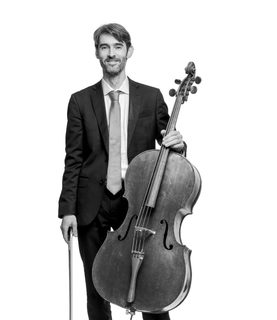 Philip stands with his cello. He wears a dark suit and white shirt.