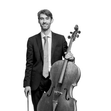 Philip stands with his cello. He wears a dark suit and white shirt.