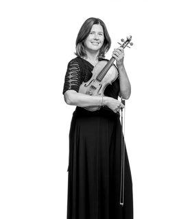 Aisling stands and smiles holding her violin. She wears a long black dress.