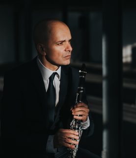 Maximiliano Martín sits in a dimly lit room, holding his clarinet and looking thoughtfully to his left.
