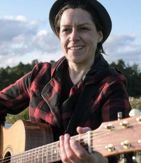 Jenny wears a hat and plays the guitar outside.