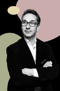 Gavin Reid stands with arms crossed. Black background and coloured blobs feature in this.