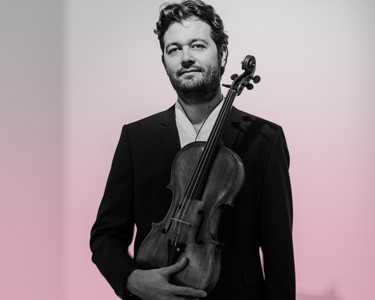 Lawrence Power holds his viola. He wears a black suit.