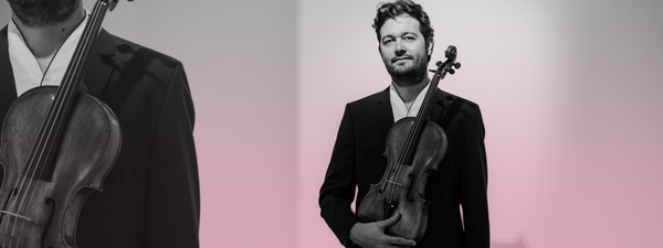 Lawrence Power holds his viola. He wears a black suit.