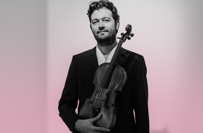 Lawrence Power holds his viola. He wears a black suit.