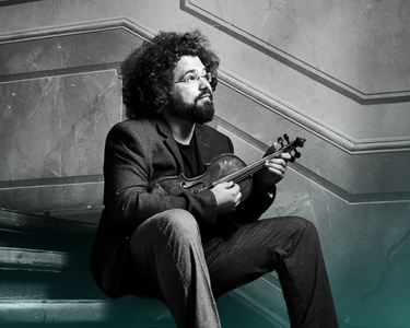 Jonian Ilias-Kadesha sits on some old stairs with a violin.