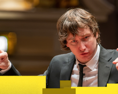 Maxim conducts in a black suit and white shirt.