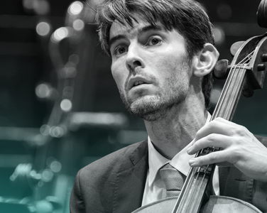 Philip Higham plays the cello. He wears a suit.