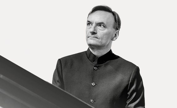 Sir Stephen Hough wears a black shirt and looks off to the right at his piano.