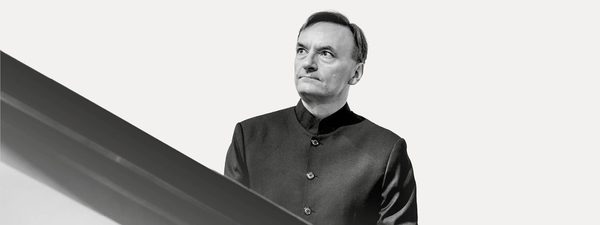 Sir Stephen Hough wears a black shirt and looks off to the right at his piano.