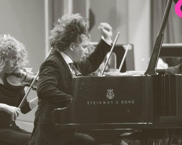 Maxim passionately plays the piano while the orchestra play behind