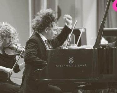 Maxim passionately plays the piano while the orchestra play behind