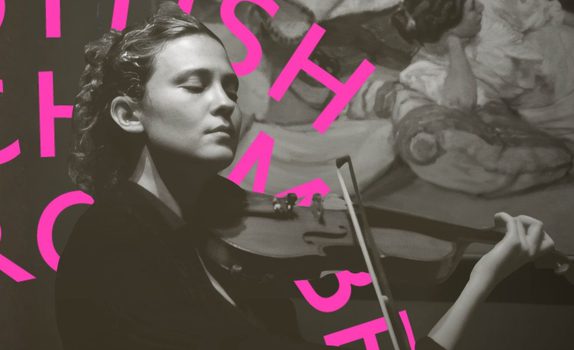 Lorenza plays her violin in front of a painting. Her eyes closed.