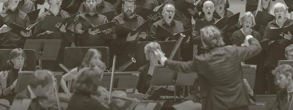 Maxim conducts the orchestra with the chorus singing behind.