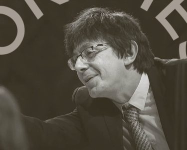 Vaclav Luks conducts. He points off to the right. He wears a patterened tie, glasses and a black jacket.