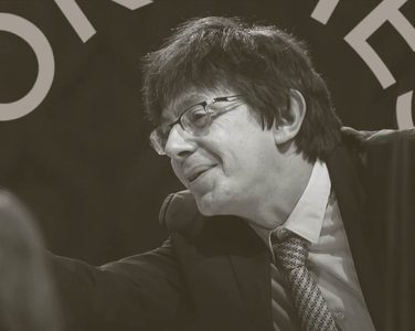 Vaclav Luks conducts. He points off to the right. He wears a patterened tie, glasses and a black jacket.