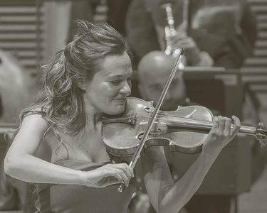 Benedetti smiles as she plays the violin. She weard a sleeveless light dress.