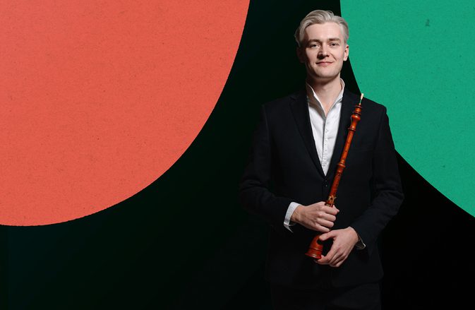 Ivan Podyomov smiling, and holding his oboe, against a dark background with bright blue, red, and green shapes.