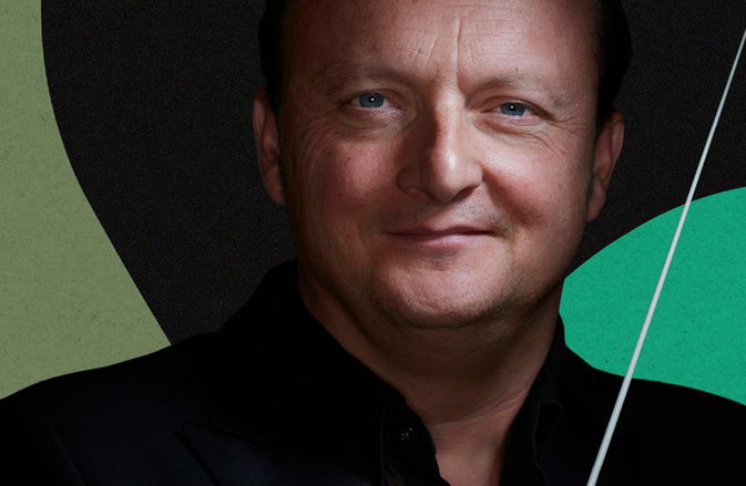 Conductor François Leleux smiling at the camera, holding the baton, against a dark background with shapes in different shades of green.