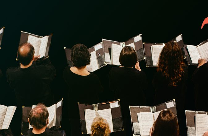 Chorus members photographed from above, holding their sheet music.